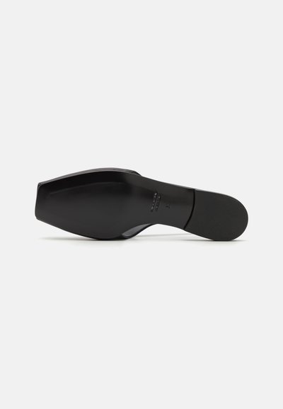 Svart högklackad sko med spetsig tå, platt bas, slät läderstruktur och minimala designfunktioner. Sulan är något böjd.