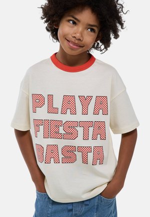 T-shirt à manches courtes crème avec col côtelé rouge. Présente un grand texte en damier rouge : "PLAYA FIESTA BASTA" avec des contours noirs en gras.