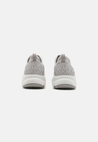Pár světle šedých slip-on tenisek s bílou podrážkou, označených opakujícím se vzorem "MK" na zadní straně a poutkem na patě.