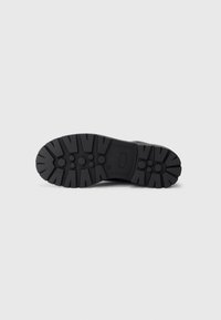 Suela de bota de goma negra con patrones de tracción profundos, agarres hexagonales y puntera reforzada para durabilidad y estabilidad.