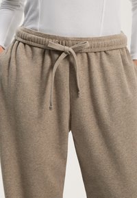 Beige-huopaidat, joissa on joustava vyötärö ja naru. Pehmeä, teksturoitu kangas, jossa on sivutaskut kätevyyden vuoksi.