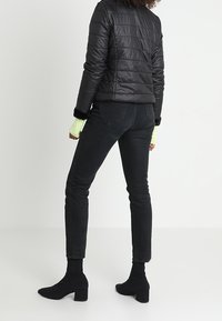 Svart puffjacka med horisontellt quiltat mönster, ihopparad med figursydda svarta jeans. Modellen bär svarta ankelboots och limegröna manschetter.