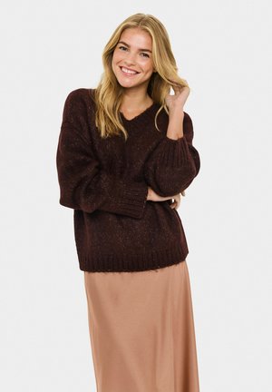 Maglione lavorato a maglia bordeaux con scollatura a V, maniche oversize e orlo a costine; abbinato a una gonna liscia marrone chiaro, lunga fino alla caviglia.