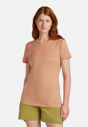 Persikofärgad t-shirt med kort ärm, tillverkad av mjukt tyg, med en konturtryck av ett tält och en eld på bröstet. Buren med gröna shorts.