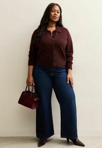 Burgundowy sweter dzianinowy z guzikami, w połączeniu z ciemnoniebieskimi spodniami o szerokich nogawkach. Dodatki to mała burgundowa torebka i czarne szpilki.