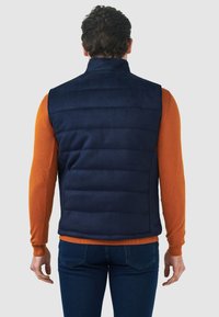 Navyblauer gepolsterter Weste mit hohem Kragen, horizontal gestepptem Design, getragen über einem orangefarbenen Langarmshirt, von hinten betrachtet.