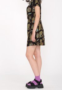 Robe noire avec des motifs de dragon colorés, à manches courtes et à coupe décontractée. Associée à des sandales noires imposantes et des chaussettes violettes.