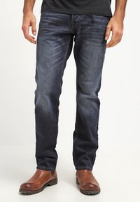 Jeans de mezclilla azul oscuro con un diseño de corte ajustado, que cuentan con un suave desgaste, estilo clásico de cinco bolsillos y costuras reforzadas.