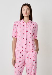 Camicetta a maniche corte con bottoni a righe rosa e bianche, con un motivo di ciliegie. Abbinata a pantaloni coordinati. Tessuto leggero e morbido.