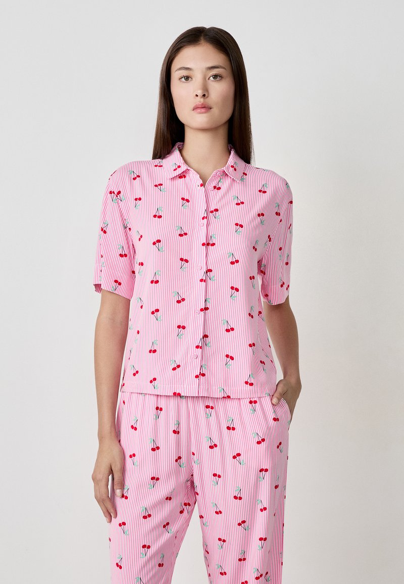 Camicetta a maniche corte con bottoni a righe rosa e bianche, con un motivo di ciliegie. Abbinata a pantaloni coordinati. Tessuto leggero e morbido.