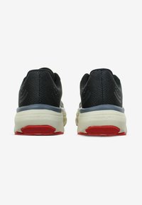 Scarpe sportive nere con una tomaia in tessuto texturizzato, suola imbottita color crema con accenti rossi e una suola esterna in gomma resistente.