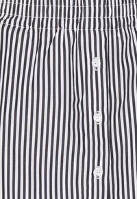 Tissu à rayures noires et blanches avec des rayures verticales, une taille élastique et des boutons blancs sur le devant. Texture lisse.