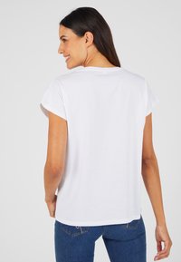 Witte kortekorte mouw t-shirt met opgerolde manchetten, een ronde halslijn en een ontspannen pasvorm, gecombineerd met blauwe jeans. Zachte katoenmateriaal.