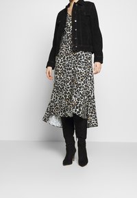 Chaqueta de ante negra sobre un vestido gris con estampado de leopardo y dobladillo asimétrico, combinado con botas altas de tacón negro.