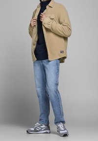 Beżowa polarowa koszula na kurtkę na granatowym golfie, do tego jasnoniebieskie dżinsy i szare sportowe buty z białymi akcentami.