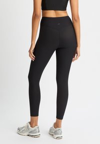 Leggings negros de cintura alta con textura acanalada, diseño ajustado y construcción sin costuras, combinados con zapatillas deportivas ligeras.