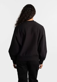 Zwarte sweatshirt met een ronde halslijn, geribbelde manchetten en zoom. De stof lijkt textuur te hebben, met een ontspannen pasvorm en een design met afhangende schouders.