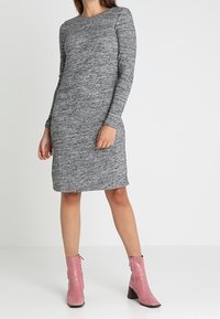 Robe cintrée à manches longues gris clair, texture douce et longueur mi-genou. Associée à des bottines roses jusqu'à la cheville avec un bout pointu.