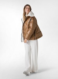 Bruine pufferjack met een glanzende afwerking, zwarte rits en een witte fleece-gevoerde capuchon. Gecombineerd met witte wijde broek en grijze schoenen.