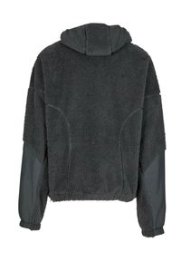 Tamsiai pilka gobtuvu fleece striukė su struktūrizuota, pūkuota išorine dalimi ir lygiomis rankovėmis. Apsaugoti elastingais rankogaliais ir laisvu siluetu.