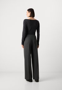 Top negro ajustado de manga larga combinado con pantalones de cuadros gris oscuro de pierna ancha y cintura alta. Textura suave, diseño a medida, patrón sutil.