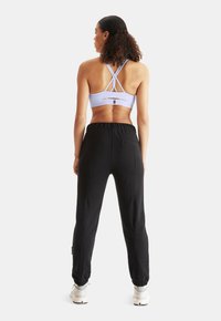 Lila sport-bh med korsryggsdesign; svarta joggers med muddade anklar och fickor; vita träningsskor. Mjuk tygtextur.