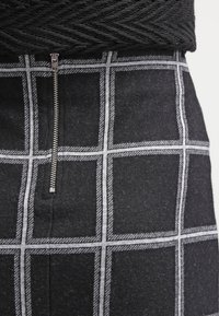 Falda de cuadros negra con cierre de cremallera, fabricada con una tela texturizada con acentos blancos en un patrón de cuadros.