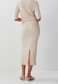 Beige koord-set med texturerad tyg. Kortärmad topp och knälång kjol med en slits bak. Slät, minimalistisk design.