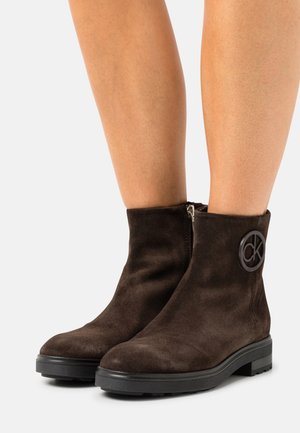 Bruna mockaskinnankelboots med rund tå, platt svart gummisula, blixtlås på sidan och en logotypdetalj på den yttre skaftet.