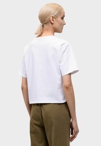 T-shirt bianco corto con maniche corte, realizzato in tessuto liscio. Il collo è rotondo e presenta un design minimale sul retro.
