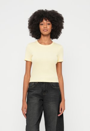 Maglietta gialla a maniche corte con coste e scollo rotondo, abbinata a jeans scuri in denim a vita alta. Tessuto liscio e taglio aderente.