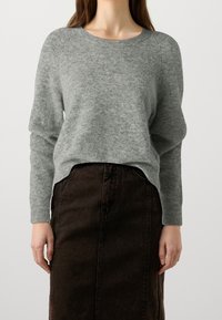 Pull gris en maille avec un col rond, des poignets côtelés et une coupe décontractée, associé à une jupe en jean marron foncé avec une couture frontale.