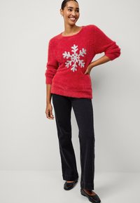 Roter, flauschiger Pullover mit einem silbernen Schneeflockenmotiv, kombiniert mit schwarzen Jeans und schwarzen Ballerinas. Dreiviertelärmel.
