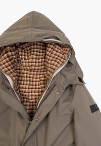 Giacca khaki con cappuccio, dotata di una fodera a houndstooth marrone texturizzato, chiusure a scatto e un'etichetta nera sulla manica.