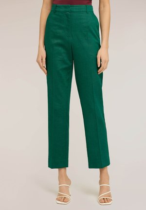 Kvinde iført højhøjede, lige ben grønne bukser kombineret med hvide, remme-sandaletter med hæl og en burgunderrød top.