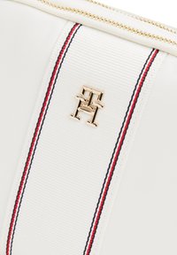 Borsa in tessuto bianco con superficie texture, con un logo dorato e strisce rosse e blu navy lungo il lato, e chiusura con zip nella parte superiore.