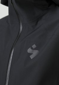 Schwarze wasserdichte Jacke mit hohem Kragen, Frontreißverschluss und dezentem Logo auf der Brust. Glatte Textur und aerodynamisches Design.