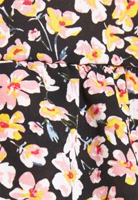 Tissu noir avec un motif floral comprenant des fleurs roses, jaunes et blanches avec des tiges vertes et des plis cousus.
