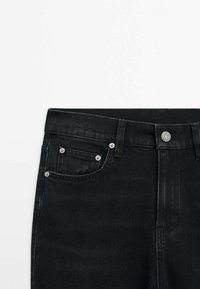 Jean en denim noir avec une taille mi-haute, deux poches avant et des garnitures argentées sur le bouton et les coutures des poches.