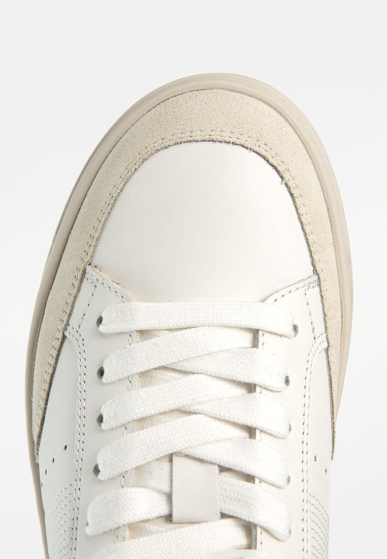 Weiße Leder-Sneaker mit einer strukturierten Wildleder-Zehenkappe, flachen weißen Schnürsenkeln und einer Gummisohle. Das Design ist schlicht und verfügt über kleine Belüftungslöcher.