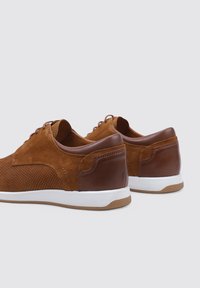 Zapatos de ante marrón con un acabado de cuero marrón suave, que cuentan con una suela de goma blanca y un diseño perforado para mayor transpirabilidad.
