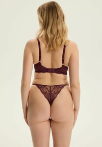 Burgunderfarbendes Spitzenunterwäsche-Set mit einem Bralette mit verstellbaren Trägern und Hakenverschluss, kombiniert mit einem passenden transparenten Tanga.