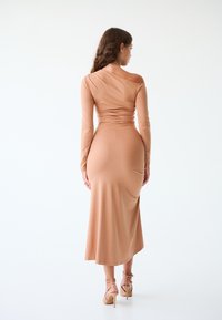 Abito midi a maniche lunghe, aderente, in morbido tessuto jersey beige, con design asimmetrico sulla spalla e dettaglio arricciato sul retro.