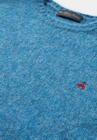 Blauer, strukturiert gestrickter Pullover aus Wolle mit Rundhalsausschnitt, schwarzes Etikett mit goldener Schrift und kleinem roten gestickten Logo in der Nähe der Brust.