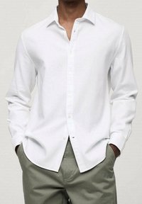 Camisa blanca de manga larga con botones y cuello clásico, hecha de una tela suave, combinada con pantalones de color verde claro, que presentan un ajuste relajado.