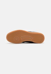 Čierna podrážka športovej obuvi s textúrovaným gumeným povrchom, s okrúhlym logom Reebok a geometrickým vzorom pre lepšiu trakciu.