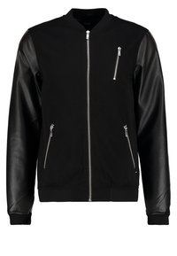 Chaqueta bomber negra con cuerpo de algodón y mangas de cuero, cuatro bolsillos con cremallera, puños de canalé y cuello redondeado.