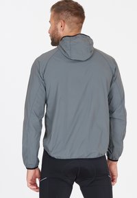 Leichte graue Windjacke mit Kapuze, ausgestattet mit elastischen Bündchen und einem taillierten Design. Glatte Textur und minimalistischer Stil.