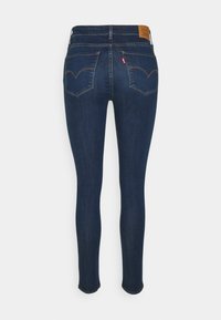 Jeans ajustados de denim azul oscuro con una textura suave, que cuentan con dos bolsillos traseros y una etiqueta de logo distintivo en la cinturilla.