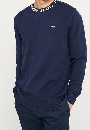 Maglione lavorato a maglia blu navy con texture a coste, colletto rotondo con una banda logo. Piccola patch con logo sul lato sinistro del petto.